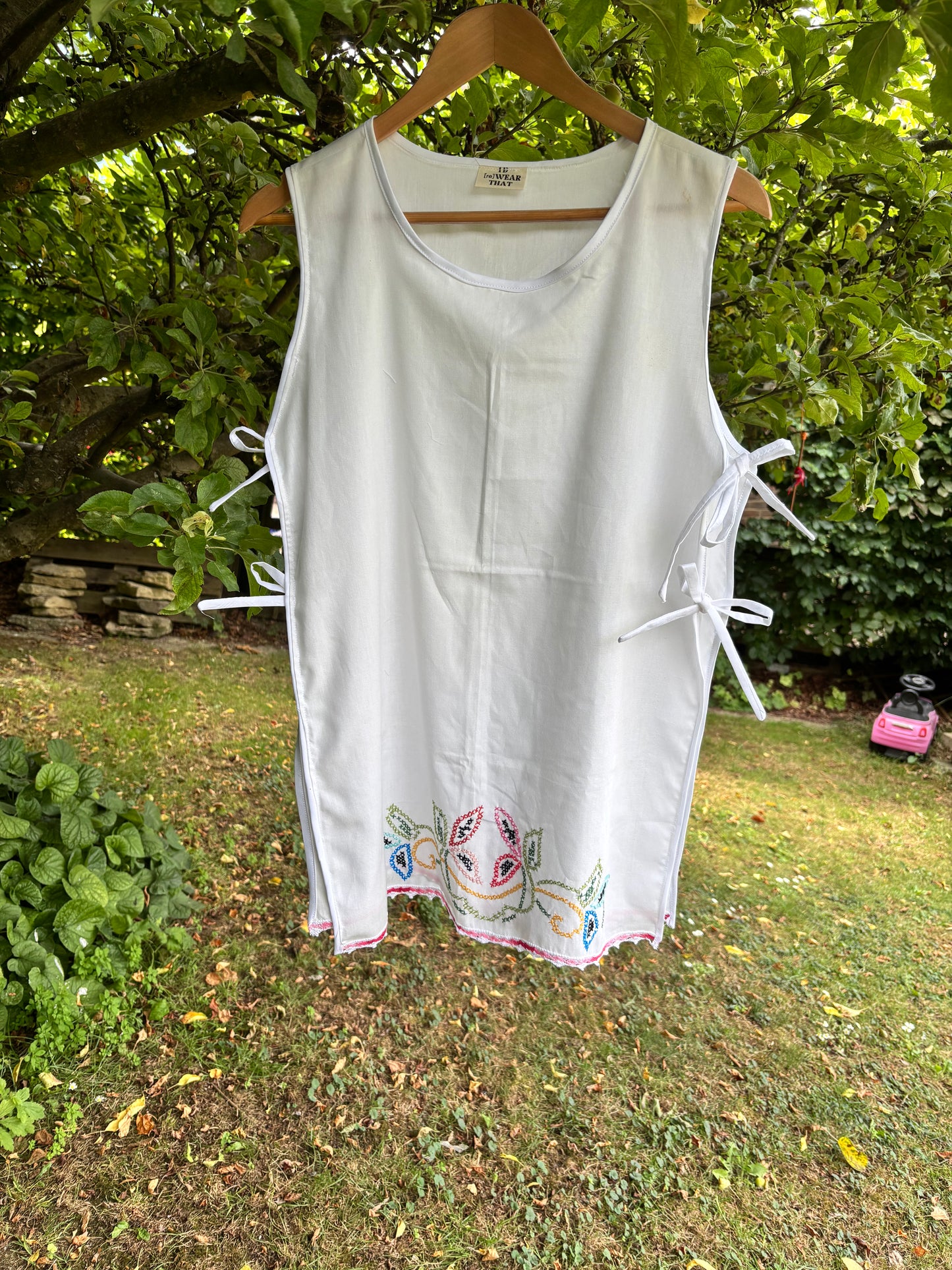 White sleeveless top with colorful embroidery on a hanger against a natural background
