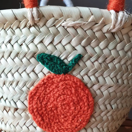 Close up of mini woven basket with an embroidered orange decoration on the front