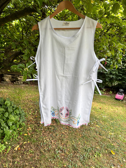 White sleeveless top with colorful embroidery on a hanger against a natural background