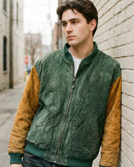 Man wearing a green and brown jacket leaning against a brick wall.