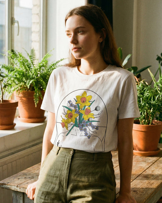 A woman wearing a white t-shirt with a daffodil and forget-me-not design in a room with plants in terracotta pots