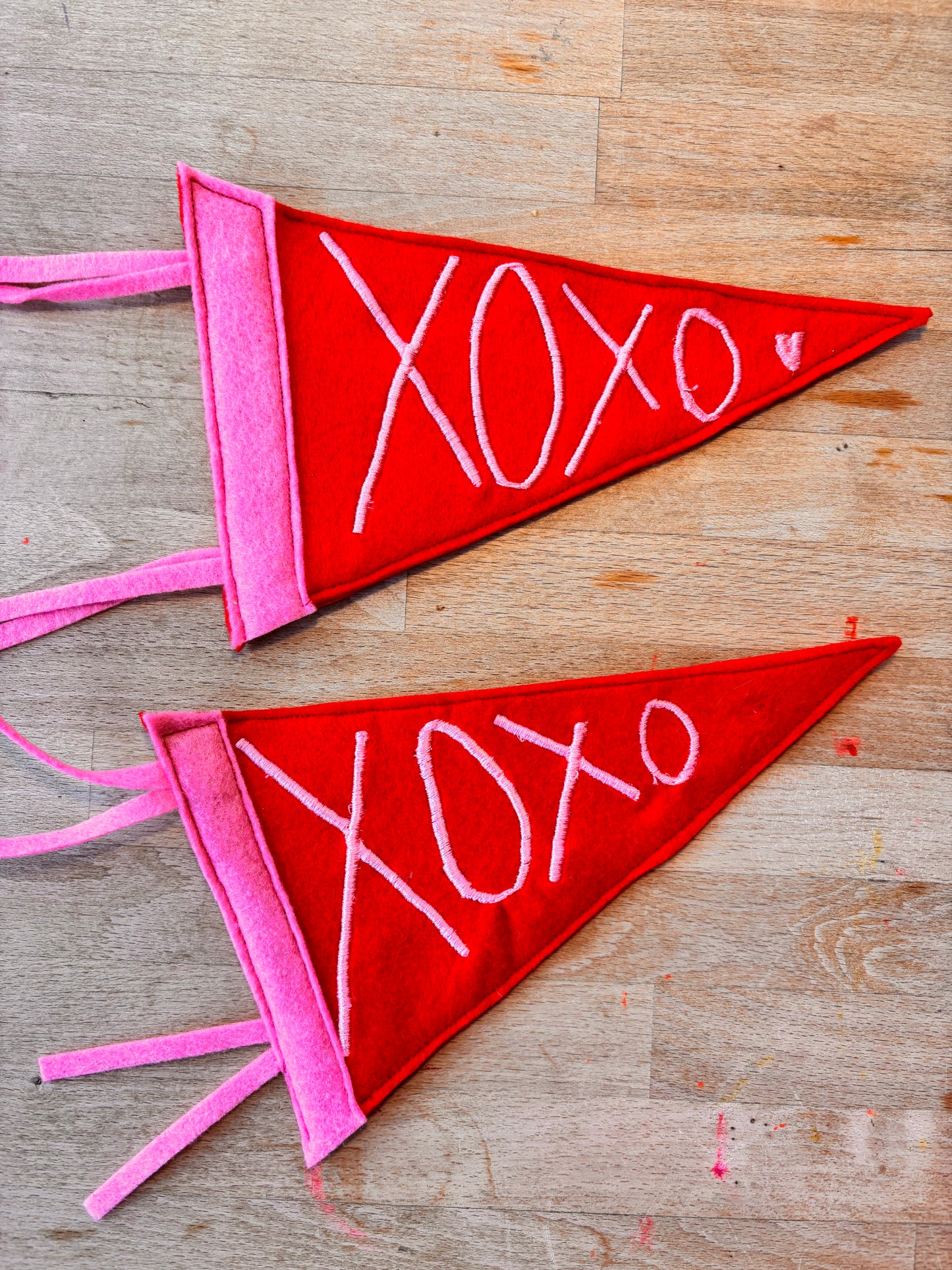 Two red and pink pennant triangular flags with 'XOXO' embroidered in pink thread.