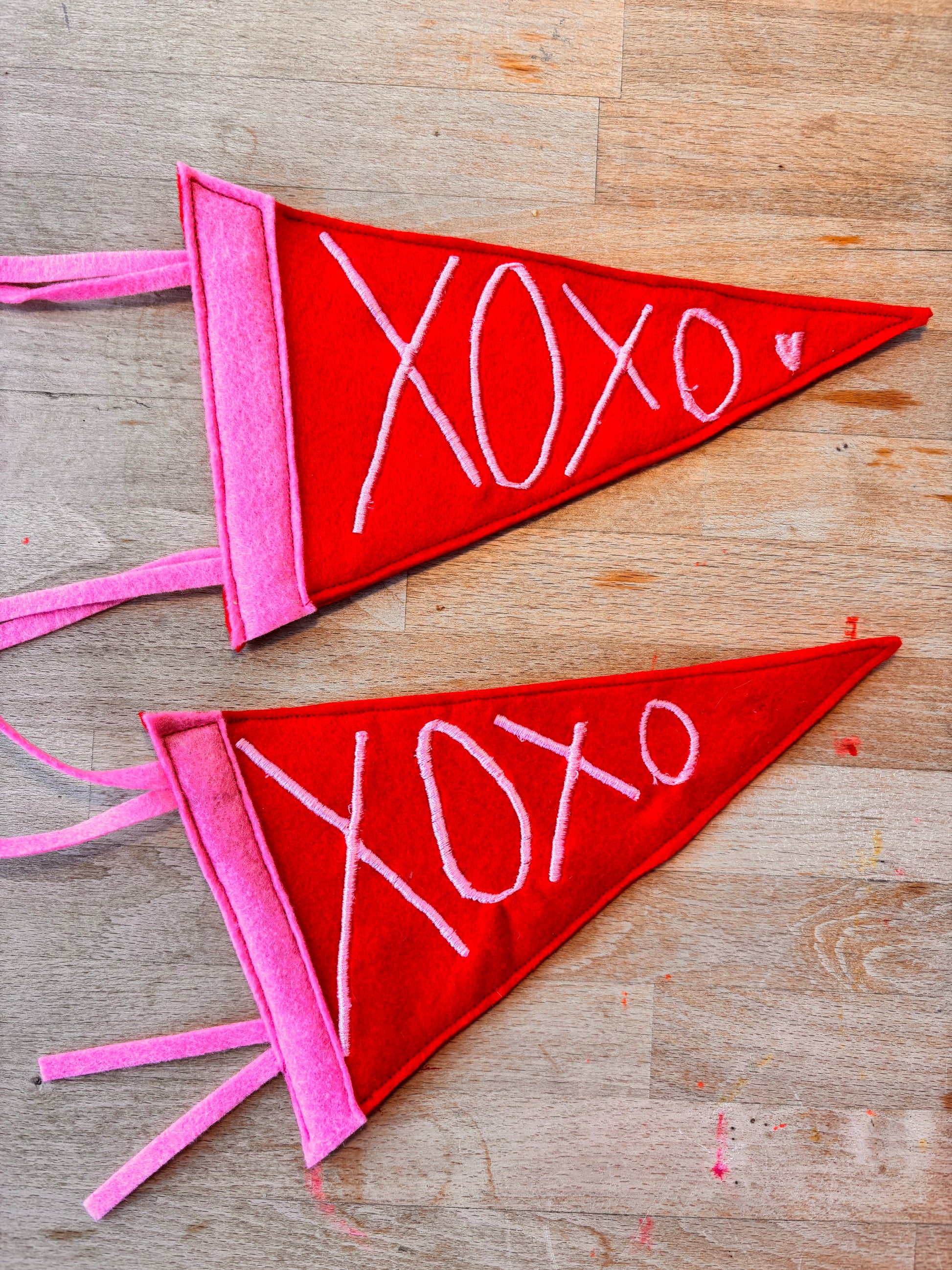 Two red and pink pennant triangular flags with 'XOXO' embroidered in pink thread.