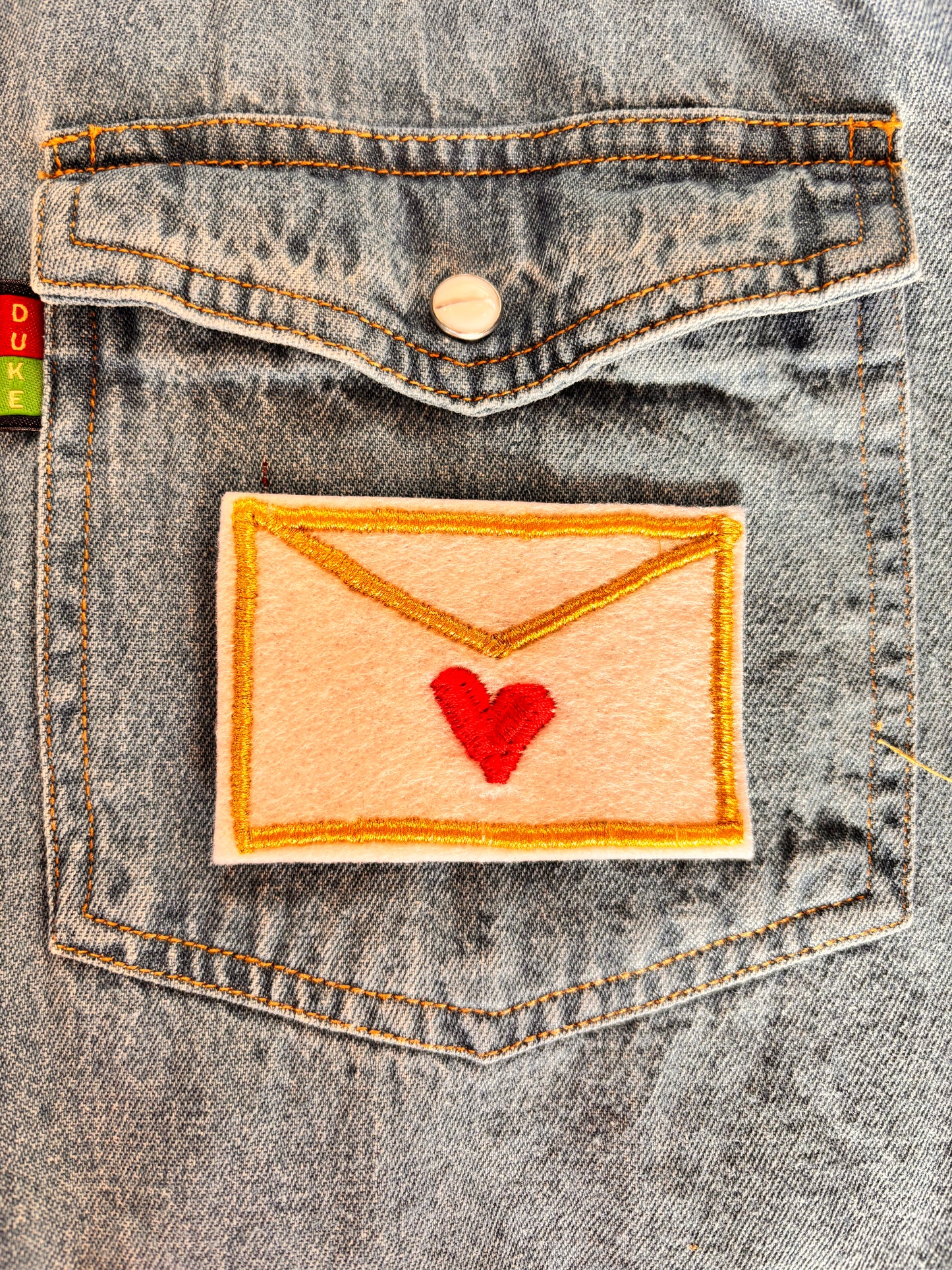 Love letter embroidery patch with a red heart attached to a denim shirt pocket