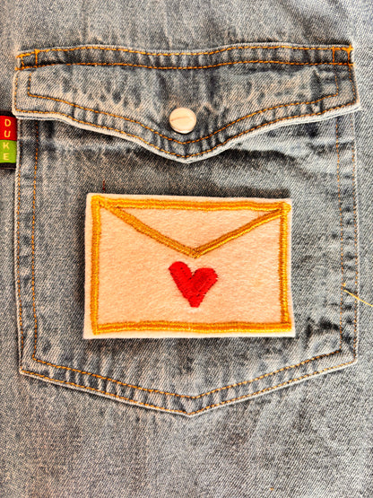 Love letter embroidery patch with a red heart attached to a denim shirt pocket