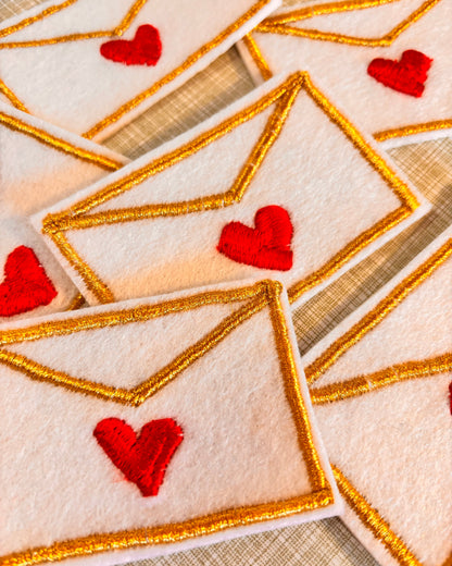 Close-up of embroidered love letter iron on embroidery patches with red hearts and gold borders.