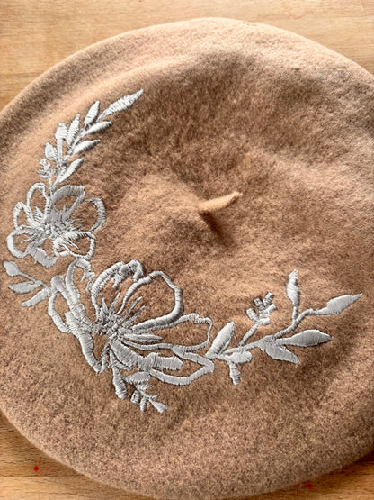 Brown beret with floral embroidery on a wooden surface