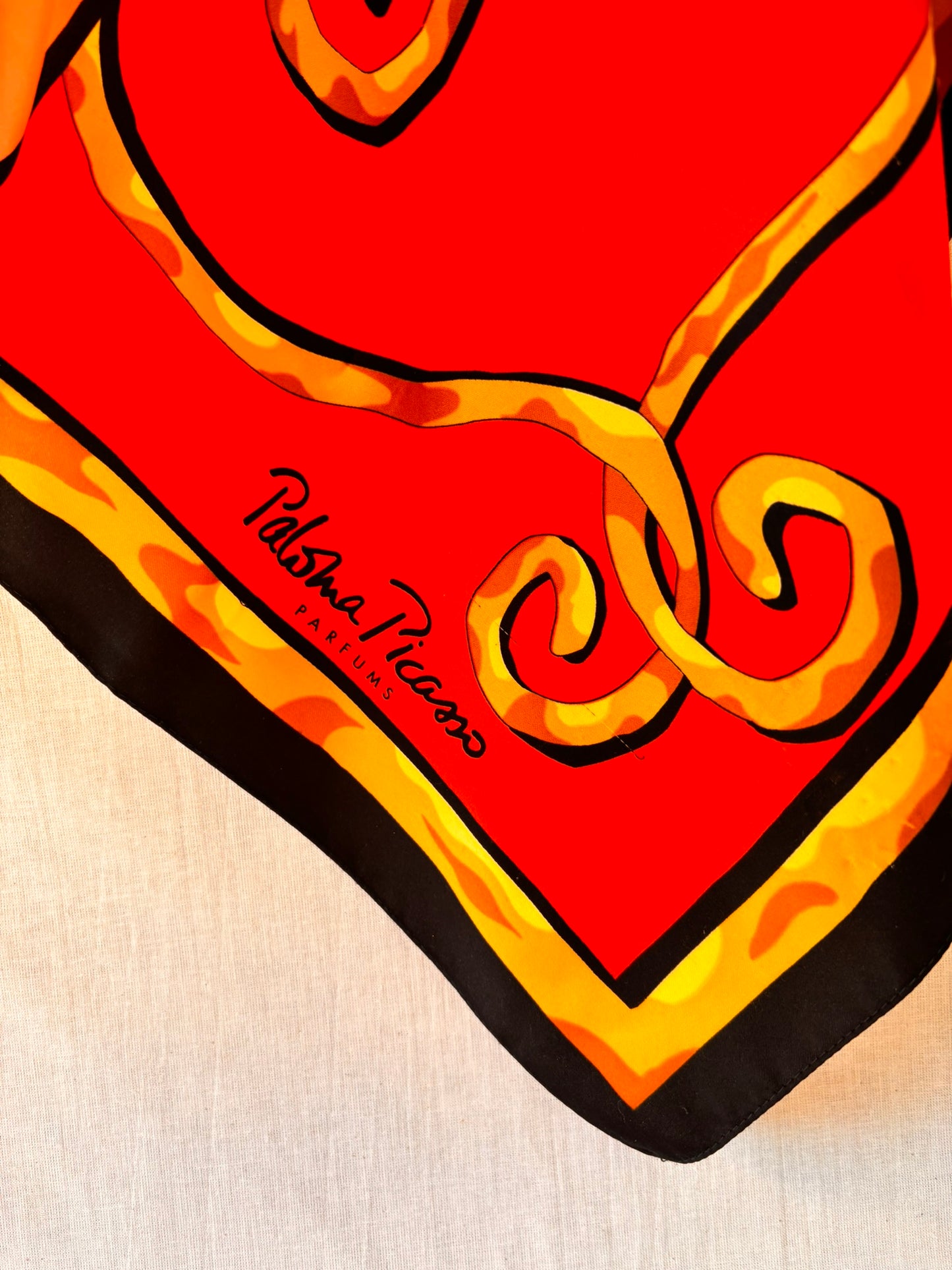 Red scarf with gold patterns and 'Pablo Picasso' branding on a beige background