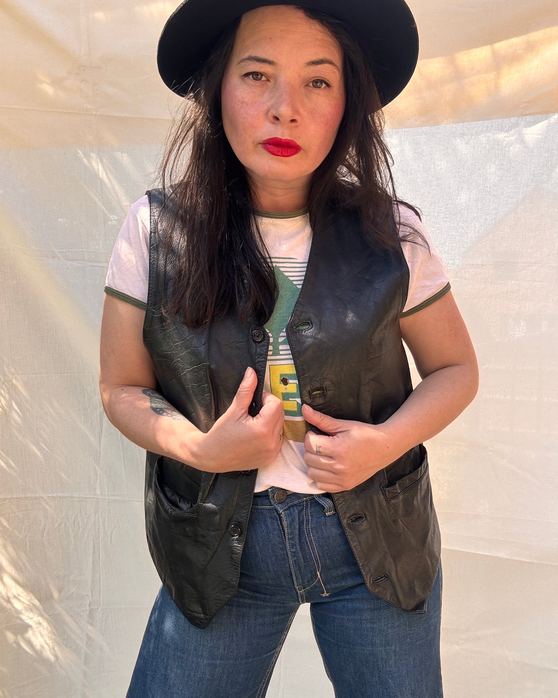 Woman wearing a black leather vest, white t-shirt, and blue jeans against a plain background