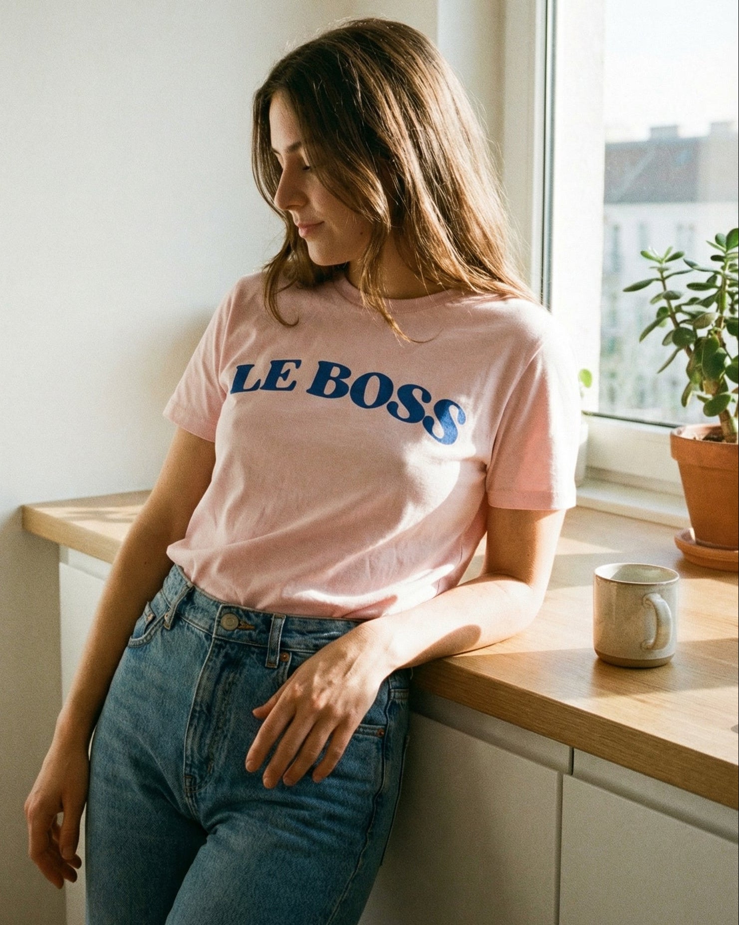 A woman wearing a pink 'LE BOSS' t-shirt is leaning against a kitchen counter.