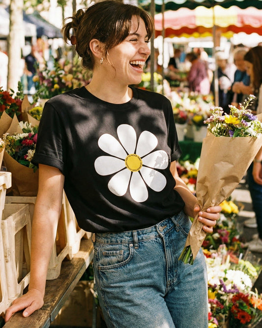 Woman wearing a black t-shirt with a white flower design at an outdoor market.